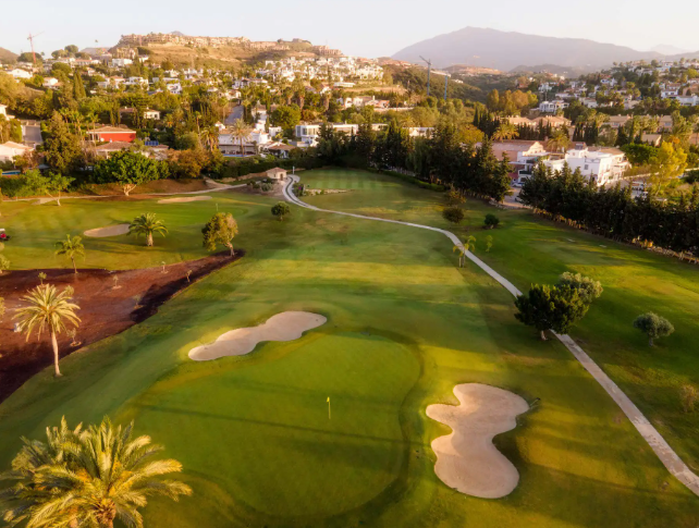 Luchtfoto van golfbaan in Estepona omringd door heuvels en villa’s